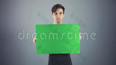 穿着黑色衬衫、拿着绿色钥匙片海报、灰色背景的年轻人