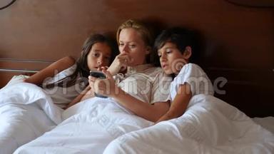 一个幸福的家庭躺在床上看着他们的智能手机上的东西。 4K，慢动作。