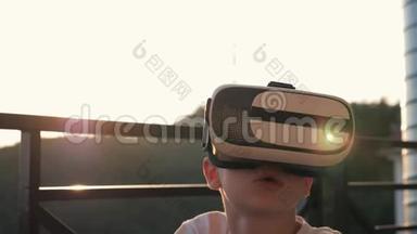 这个男孩正在电脑上玩虚拟现实眼镜在日落时。 现代概念