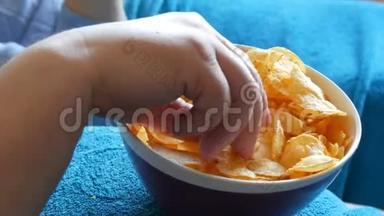 已婚夫妇躺在一张蓝色毯子下面的沙发上，吃着站在一个大肚子上的盘子里的薯片