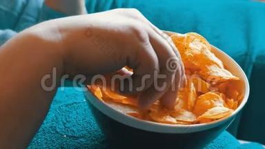 已婚夫妇躺在一张蓝色毯子下面的沙发上，吃着站在一个大肚子上的盘子里的薯片