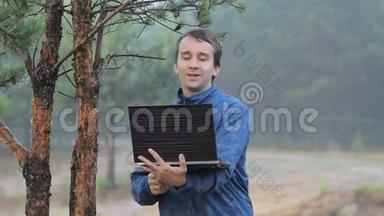 一个男人在森林里一棵树旁的笔记本电脑上打视频电话。清晨