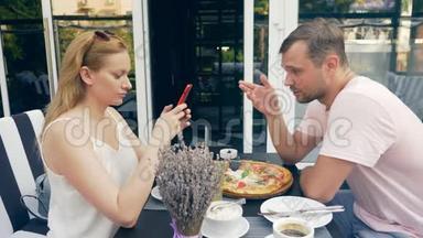一对在户外咖啡馆。 男女约会。 一个搭档看着他的手机，第二个试图和他说话。 4k