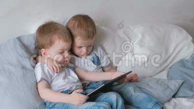 带平板电脑的孩子。 两个男孩双胞胎蹒跚学步，看着躺在床上的平板电脑。