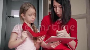 母亲和小女儿在数码平板电脑上网上购物时看鞋类。 网上购物的概念