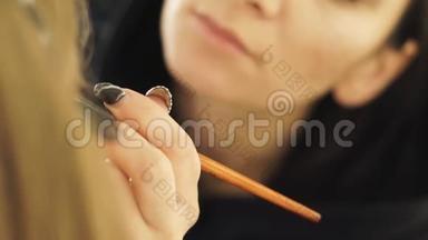 化妆设计师用画笔将化妆品应用于美容工作室的皮肤脸女时装模特上。 专业化妆