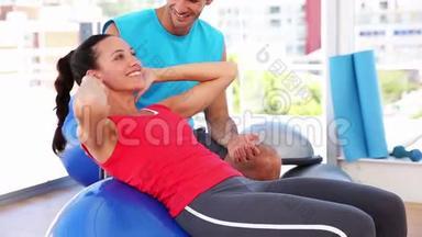 适合女人与教练一起做蓝色健身球的仰卧起坐