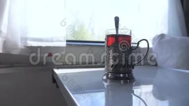 铁路旅行概念。 一杯玻璃杯中的勺子茶，老式的茶摊在火车车厢的桌子上