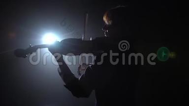 专业人士在一个黑暗的工作室里拉小提琴，灯笼从它的眩光。 黑烟背景。 背面