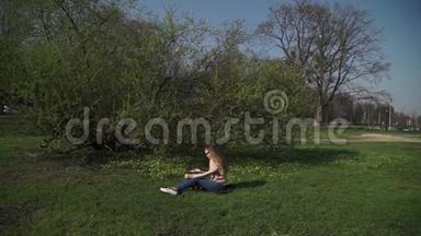 美丽的年轻女子穿着牛仔裤，在阳光下的<strong>夏日</strong>公园里，幸福地坐在郁郁葱葱的<strong>绿草</strong>中