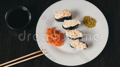 一个白色的大盘子，上面放着四个巨大的寿司黑吉里，旁边是粉红色的生姜和绿色的芥末