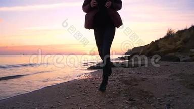 美丽的快乐女孩沿着海滩缓慢地奔<strong>跑到</strong>秋天的日落。 很冷。