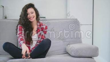 一个漂亮的女人看电视，坐在沙发上，手里拿着遥控器。