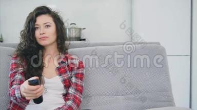 一个漂亮的女人看电视，坐在沙发上，手里拿着遥控器。