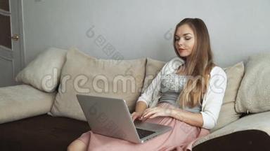 年轻女子坐在沙发上用笔记本电脑和微笑