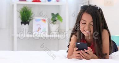 快乐的亚洲可爱女孩玩智能手机，微笑着面对家里