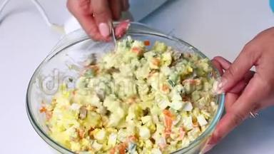 带有蔬菜和蛋黄酱的俄罗斯肉沙拉。 一个女人把蛋黄酱和沙拉的配料混合在一起。