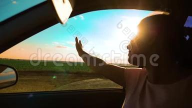 女孩挥手在窗户阳光下，风在汽车慢动作视频。 年轻快乐的女孩开汽车