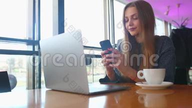 女人在咖啡馆里用智能手机打<strong>短</strong>信。 一位年轻女士坐在桌旁，用<strong>手机端</strong>着咖啡