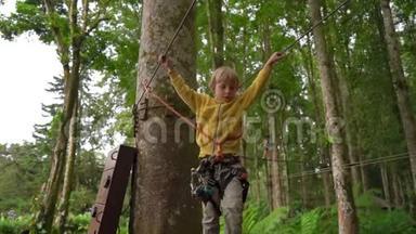 一个穿着安全装备的小男孩在森林探险公园的树梢上爬上了一条路线。 他是