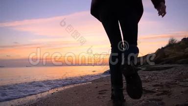 美丽的快乐女孩沿着海滩缓慢地奔跑到秋天的日落。 很冷。