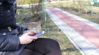 女孩打印一条信息，在春天公园的智能手机上滚动页面