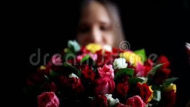 美丽的黑发女人，怀里抱着一大束花，闻着一朵芬芳的五颜六色的玫瑰花在黑色上