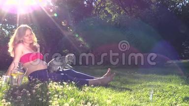 孕妇玩猫坐在阳光明媚的公园苜蓿草甸