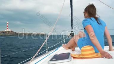 一位戴着黄色帽子，穿着蓝色裙子的女士在海洋的夏季靠近灯塔的游艇上休息