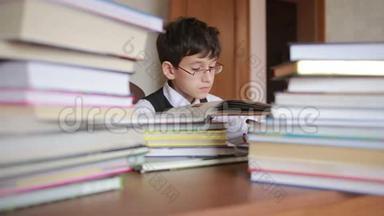 男孩坐在一张桌子旁，桌上放着一叠书。 孩子读书。 戴眼镜的男孩