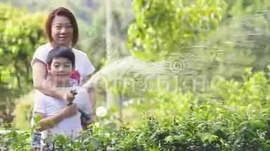 亚洲的母子正在给树浇<strong>水</strong>，<strong>站</strong>在花园里的树荫下