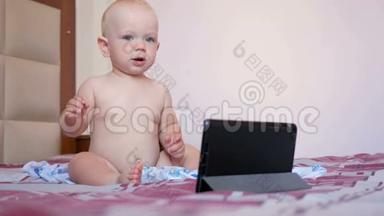 可爱的孩子坐在床上盯着平板电脑上的卡通。一岁的小婴儿，<strong>没有衣服</strong>