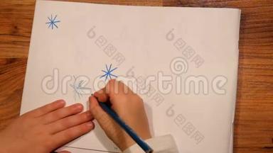 近距离观看儿童手在纸上的绘画。 用蓝色铅笔画星星。