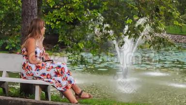 金发女郎坐在喷泉旁的长凳上，公园里有iPhone