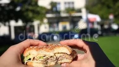 一个男人在街上吃快餐。 他穿着一个汉堡吃。 在一个模糊城市的背景下