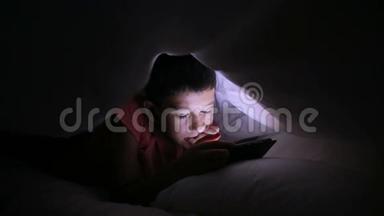 小男孩在床上玩手机或智能手机。 夜晚