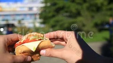 一个男人在街上吃快餐。 他穿着一个汉堡吃。 在一个模糊城市的背景下