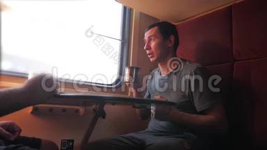 男人坐在<strong>火车车厢</strong>里，手里拿着铁路，喝着咖啡和茶。 慢动作视频。 两个人喝酒