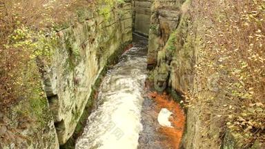 砂岩岩石之间快速满流的泡沫水，肮脏的河岸上的橙色沉积物。 深深的河床变成了岩石
