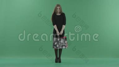 漂亮的女人穿着黑色的小裙子，摆着购物袋。 她正站在一间反对绿色的工作室里