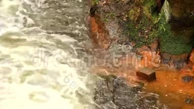 砂岩岩石之间快速满流的泡沫水，肮脏的河岸上的橙色<strong>沉积</strong>物。 深深的河床变成了岩石