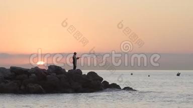 渔夫的剪影，日落时分在岩石上钓鱼