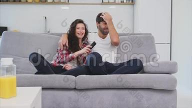 漂亮的女孩和一个年轻人坐在沙发上看电视。 人们在沙发上放松。 戴眼镜的年轻人
