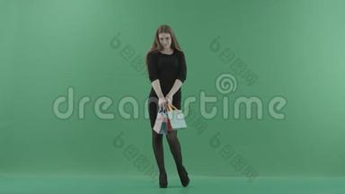 漂亮的女人穿着黑色的<strong>小裙子</strong>，摆着购物袋。 她正站在一间反对绿色的工作室里