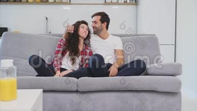 漂亮的女孩和一个<strong>年轻人</strong>坐在沙发上看电视。 人们在沙发上放松。 戴眼镜的<strong>年轻人</strong>