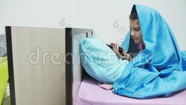 十几岁的女孩在毯子下玩智能手机。 小女孩睡前躺在室内床上上网