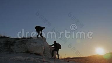 在两个登山者之间帮忙的剪影。 山顶上有两个徒步旅行者，<strong>一个人</strong>帮助<strong>一个人</strong>爬上<strong>一</strong>个纯粹的地方