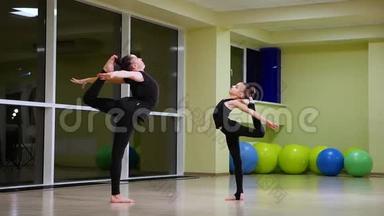 两个身材苗条、可爱的女孩姐妹，穿着黑色<strong>运动</strong>服的艺术体操<strong>运动</strong>员，在健身房做热身<strong>运动</strong>，做肌肉伸展<strong>运动</strong>