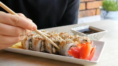 一个十几岁的男孩拿着中国竹签的寿司卷，把它放进酱油里，拿一块粉红色的生姜