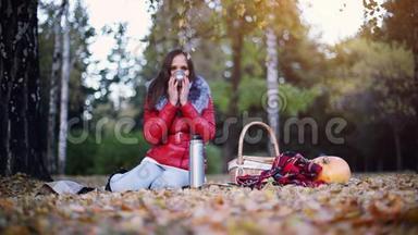 年轻女子坐在南瓜旁边野餐，在秋天公园里喝热水瓶里的热茶。 1920x1080